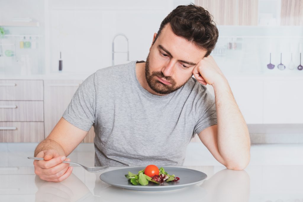 A veteran man with an eating disorder staring unhappily at a salad